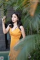 A woman in a yellow dress standing next to a palm tree.