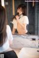 A woman in a white shirt is brushing her teeth in front of a mirror.