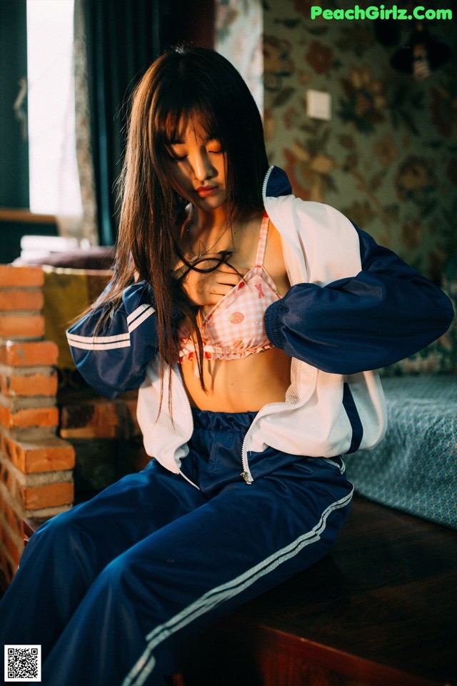 A woman sitting on a bed wearing a blue and white jacket.