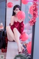 A woman sitting on a window sill holding a red balloon.