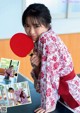 A woman in a red and white kimono holding a ping pong paddle.