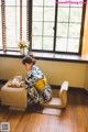 A woman in a kimono sitting on a chair in front of a window.